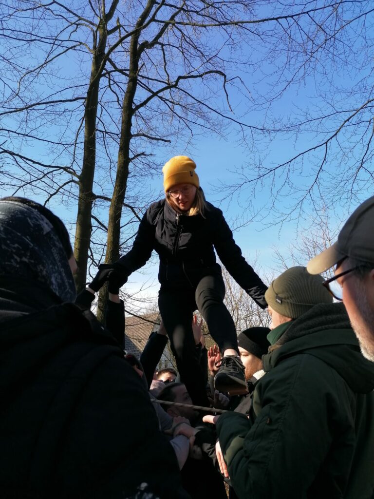 Eine junge Frau mit gelber Mütze steigt mit Hilfe von weiteren Personen über ein Seil