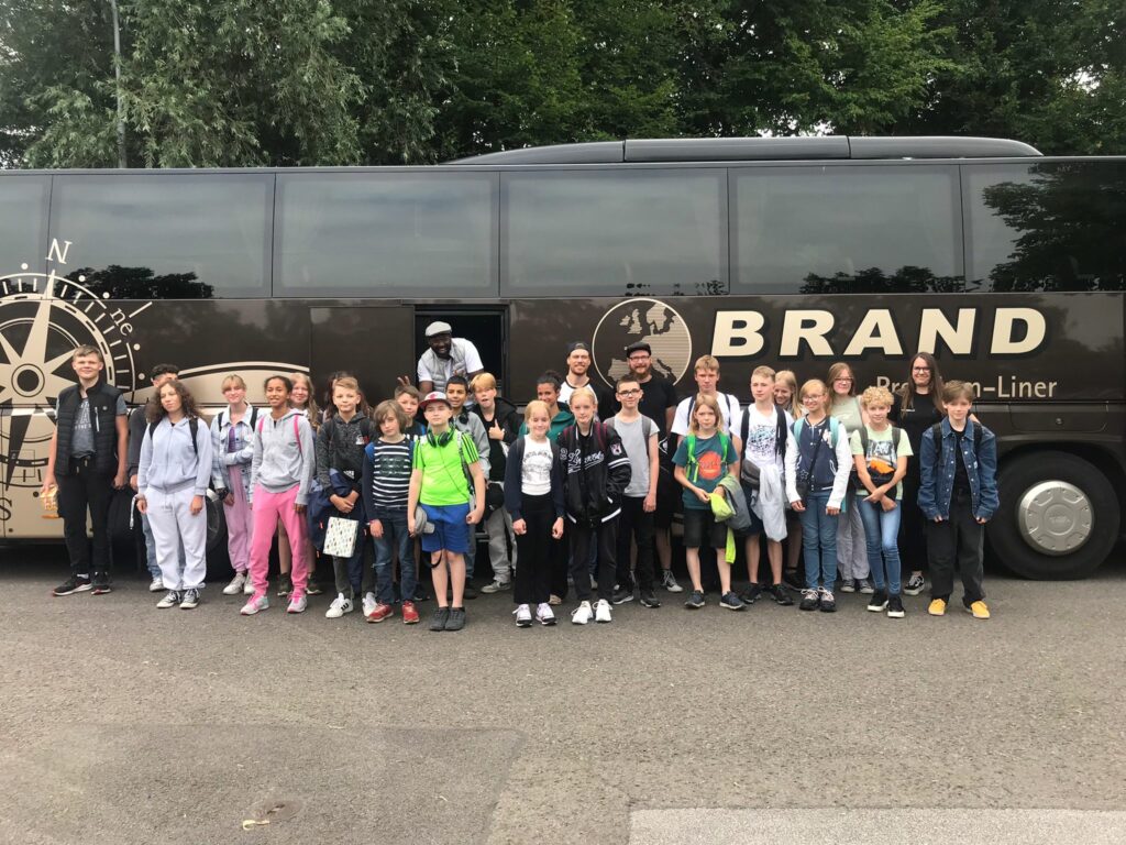 Eine Gruppe Kinder steht von einem großen dunkelbraunen Reisebus und posieren für das Foto