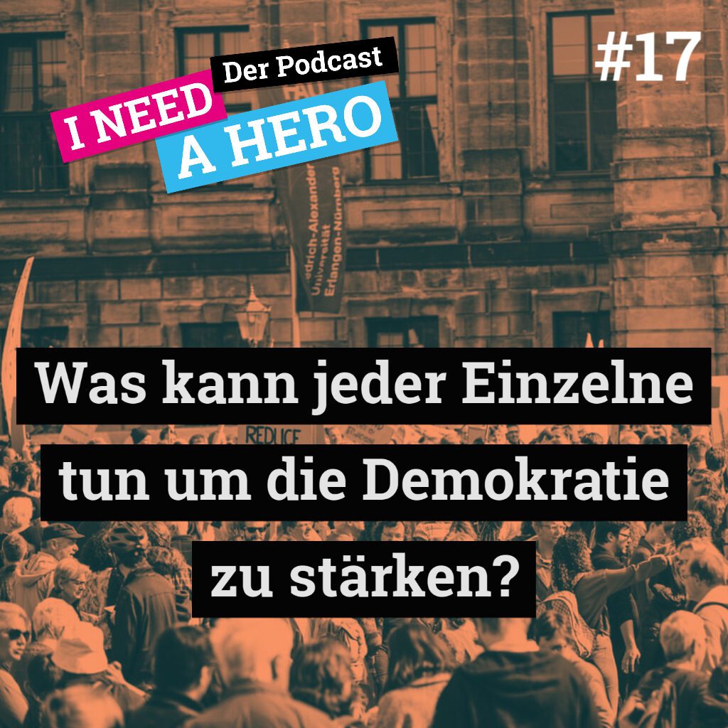 Eine Menschenmasse vor Gebäude. Unten mittig Schriftzug "Was kann jeder Einzelnde tun um die Demokratie zu stärken?". Links oben Schriftzug in verschienenen Farben: "I need a Hero - Der Podcast"