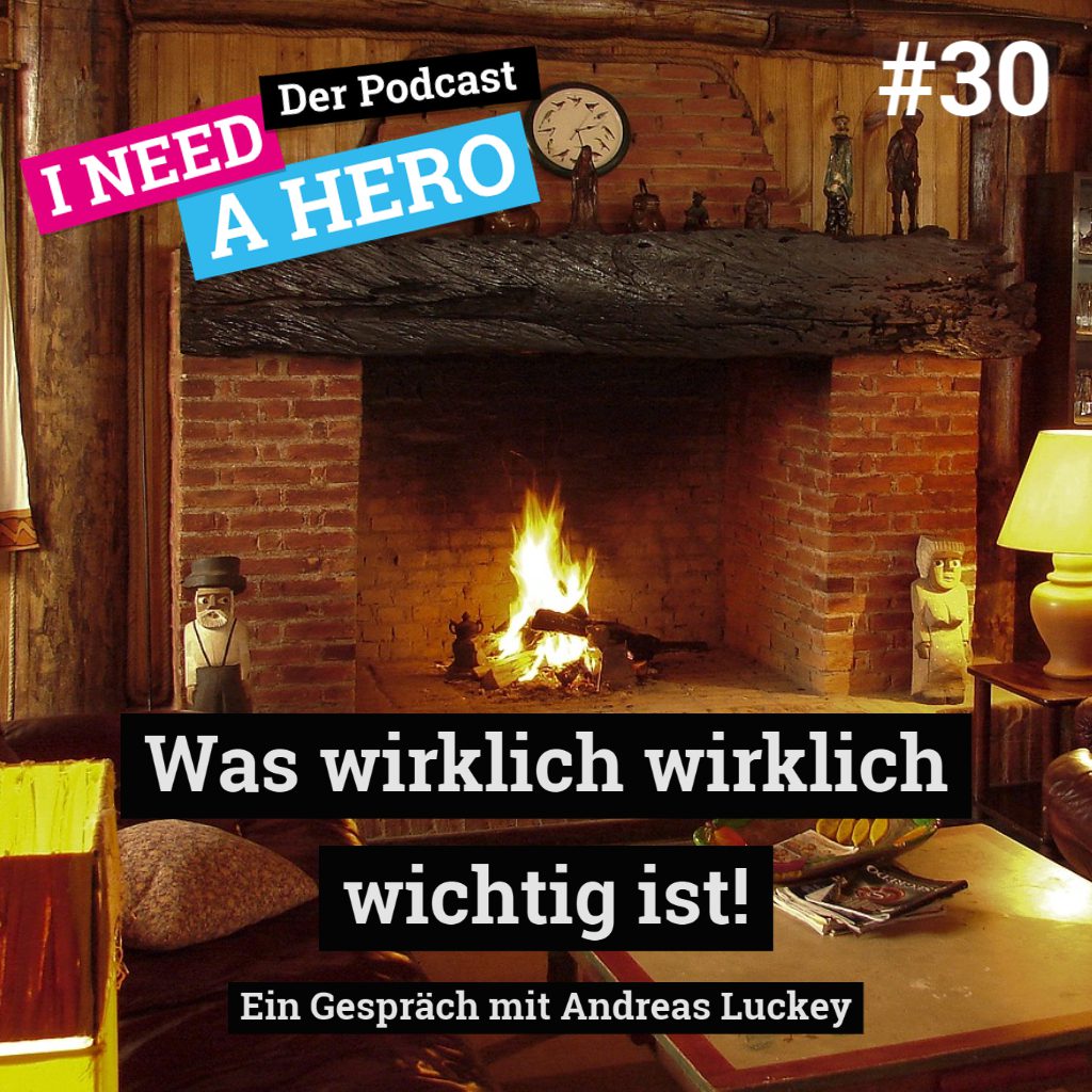 Raum mit Kamin, braunem Ledersofa und Holztisch. Unten mittig Schriftzug "Was wirklich wichtig ist!". Links oben Schriftzug in verschienenen Farben: "I need a Hero - Der Podcast"