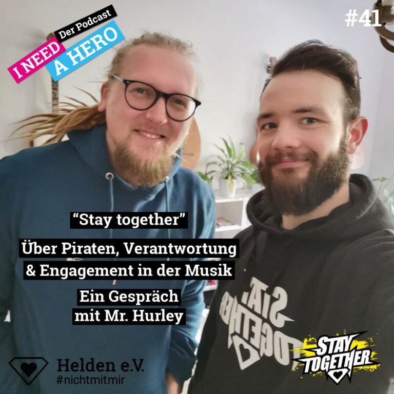 Zwei Männer mit Hoodie schauen freundlich. Unten mittig Schriftzug "Über Piraten, Verantwortung & Engagement in der Musik". Links oben Schriftzug in verschiedenen Farben: "I need a Hero - Der Podcast"