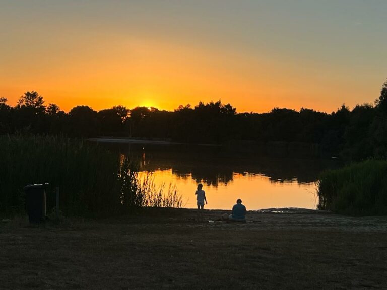 Rückansicht zwei Personen bei Sonnenuntergang am Badesee