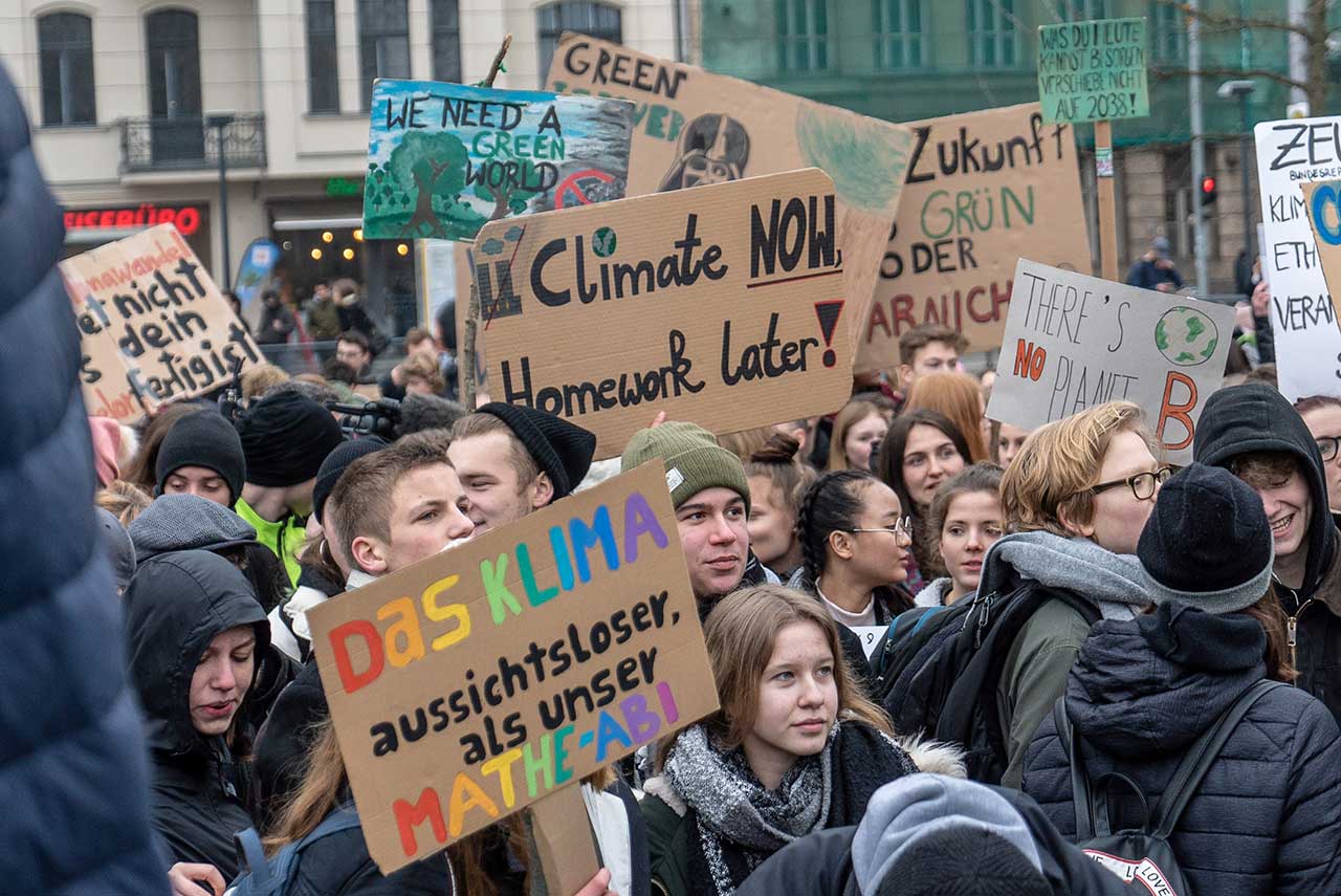 Eine Fridays-For-Future Demonstration in welcher Jugendliche beschriftete Pappschildern mit klimaaktivistischem Inhalt in die Luft halten.
