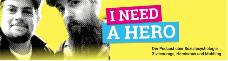 Auf gelbem Grund sind links neben dem Schriftzug: "I NEED A HERO" zwei junge Männer abgebildet der eine schaut fröhlich der andere ausdruckslos den Betrachter an.