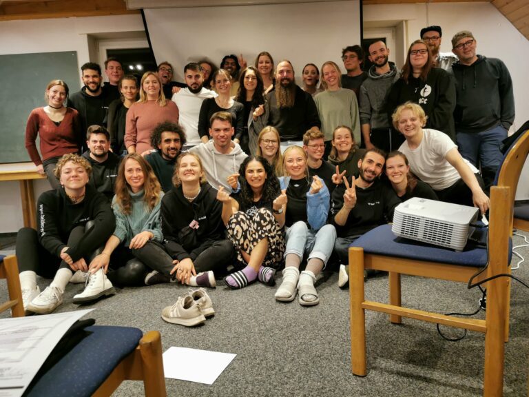 Gruppe junger Menschen in einem Seminarraum schauen lächelnd in die Kamera und posieren für ein Foto.