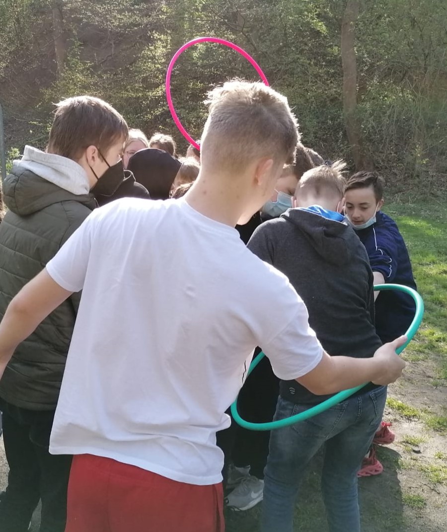 Eine Gruppe Jugendlicher die mit zwei Hula Hoop Reifen draußen ein Spiel spielen