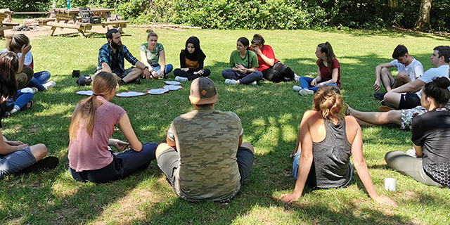 Eine Gruppe junger Menschen sitzt in einem Kreis auf einer Wiese