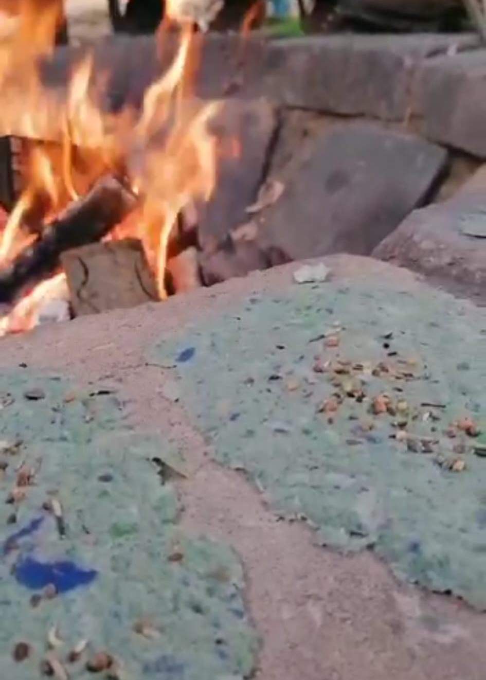 Nahaufnahme zwei Samenpapiere auf Stein liegend. Im Hintergrund brennt ein Lagerfeuer.