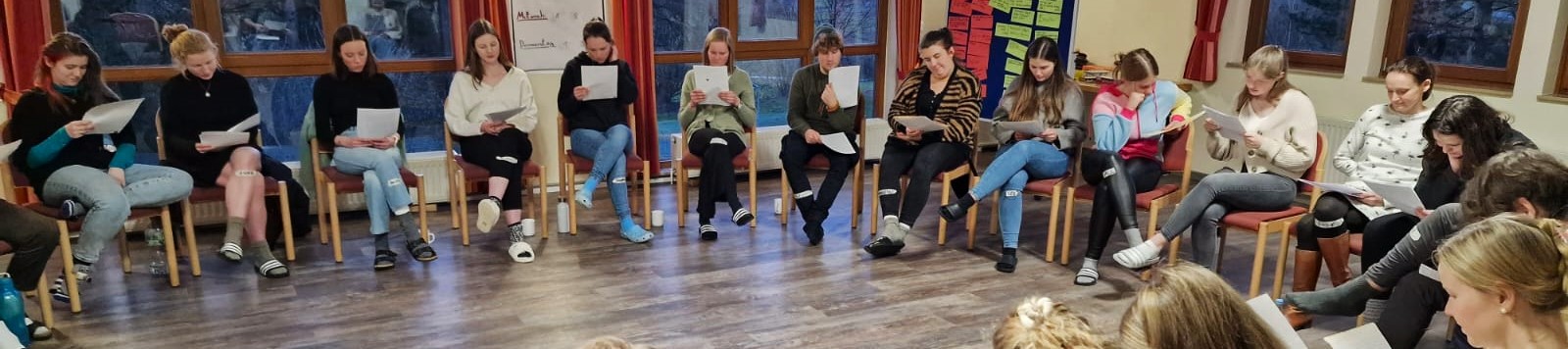 Eine Gruppe Junger Menschen sitzt in einem Stuhlkreis und liest Briefe