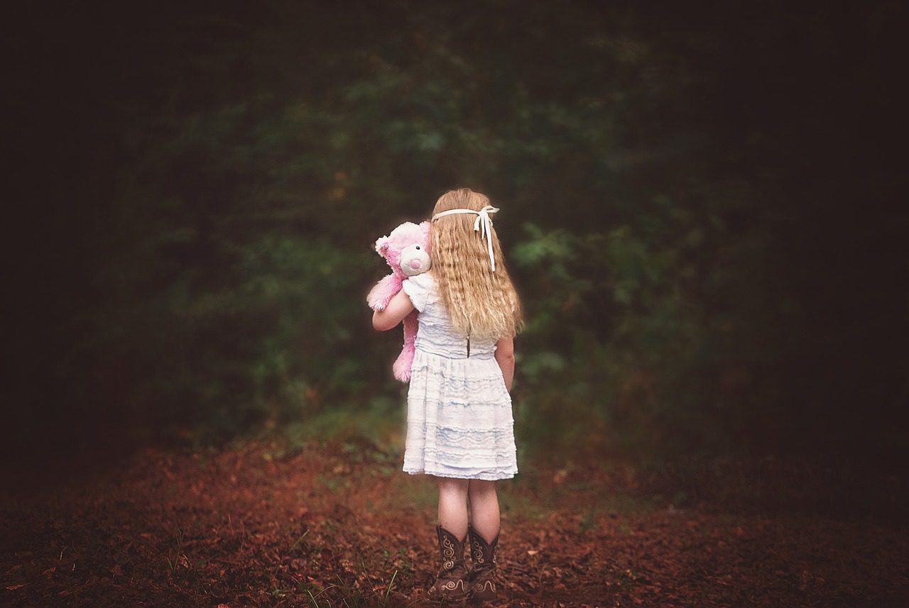 Mädchen steht einsam mit Teddybär im Wald. Ein Ausdruck von Verlustangst.