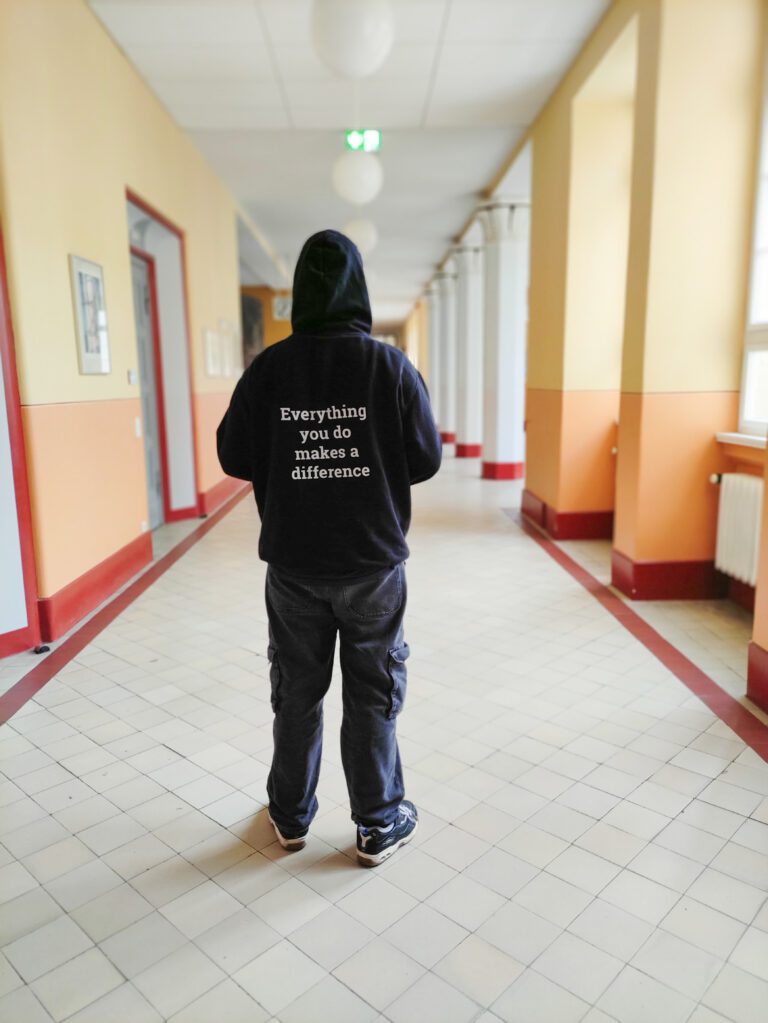 Person mit Helden e.V. Pullover steht im Gang einer Schule.