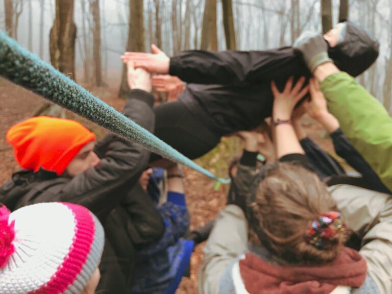 Person wird bei einer erlebnispädagogischen Teamaufgabe von anderen über ein Seil gehoben.